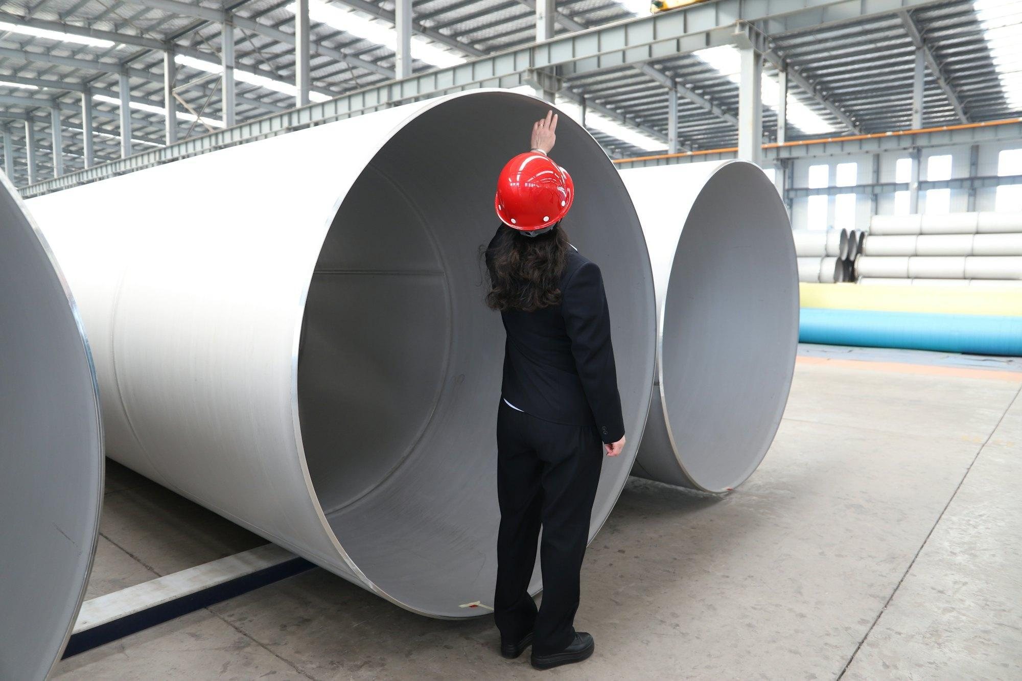 Engineer in a red hard hat inspecting large-diameter pipes